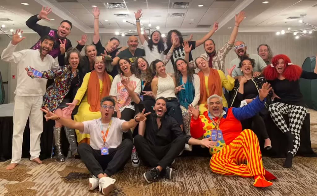 Grupo de participantes y clowns celebrando con los brazos en alto al cierre de un encuentro